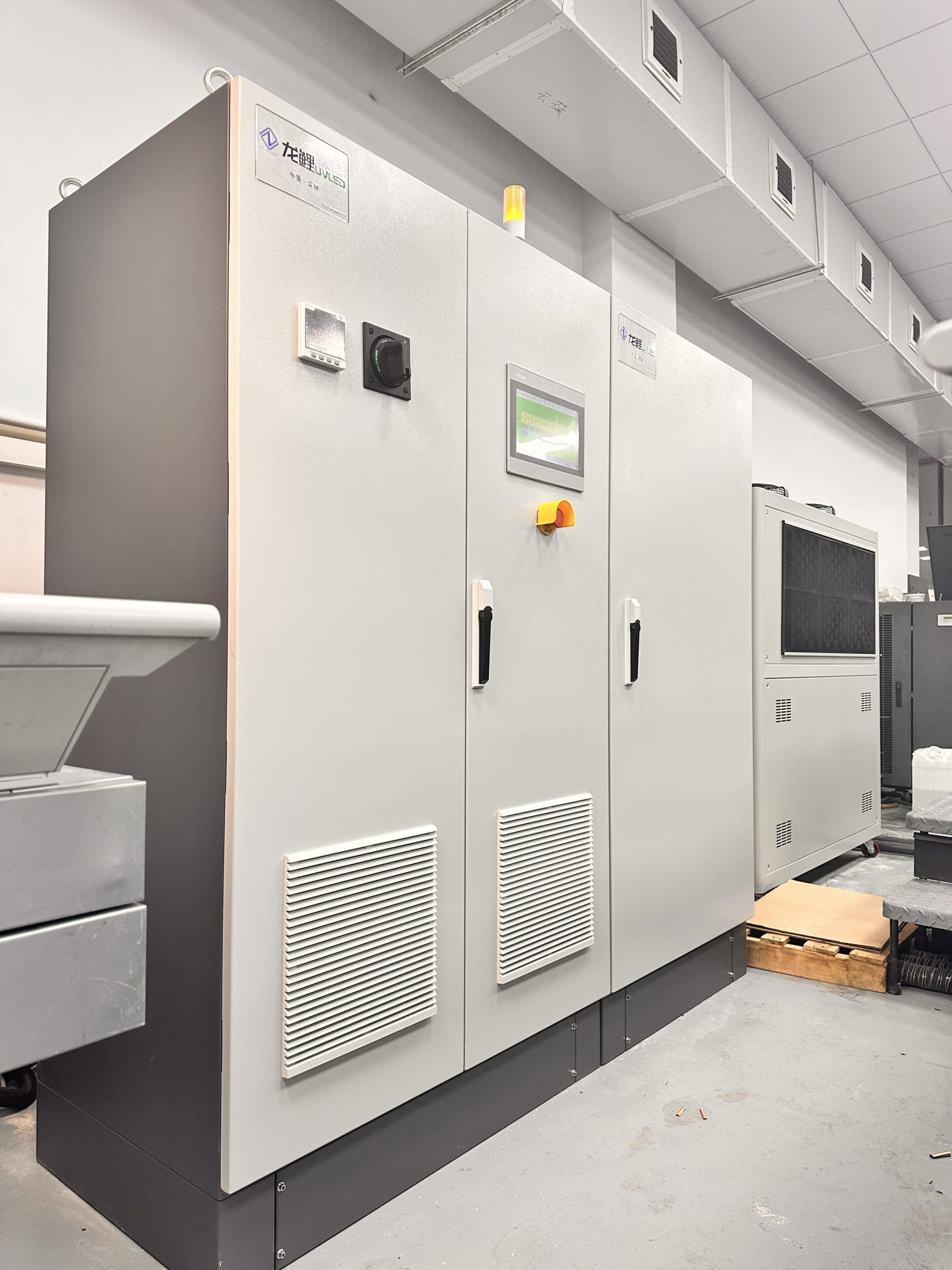 Installed UV LED curing cabinet system with ducting and auxiliary cooling equipment beside an industrial press.